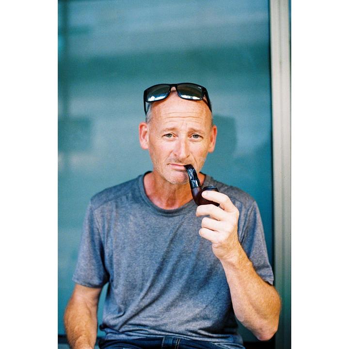 A man with sunglasses on his head holds a pipe to his mouth.