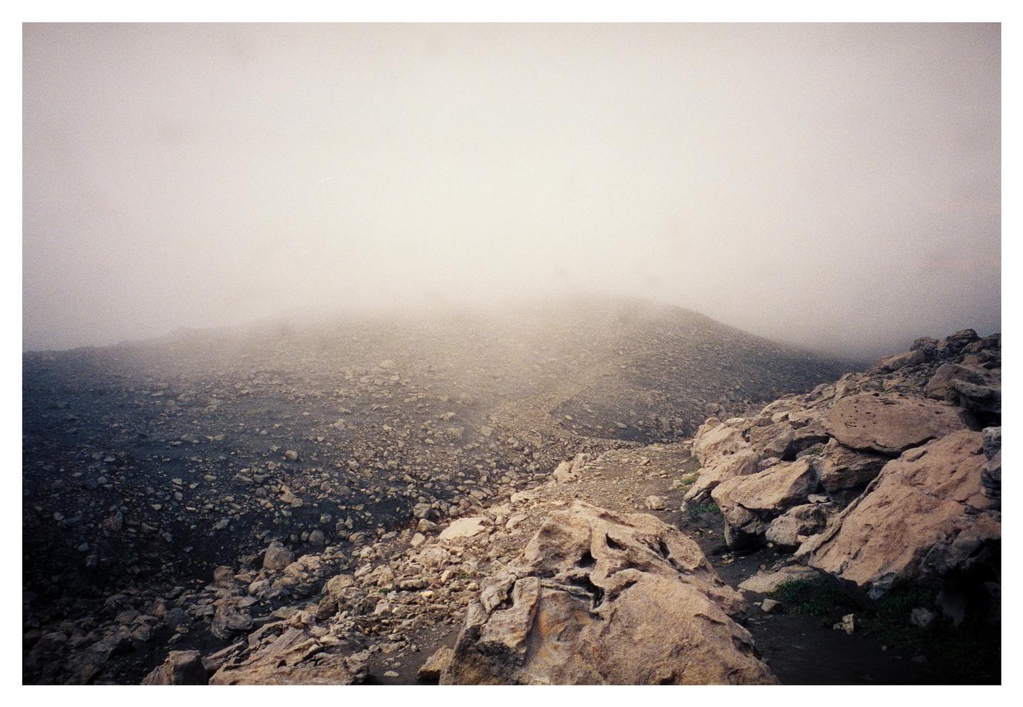 A rocky, barren landscape is covered in a thick fog.