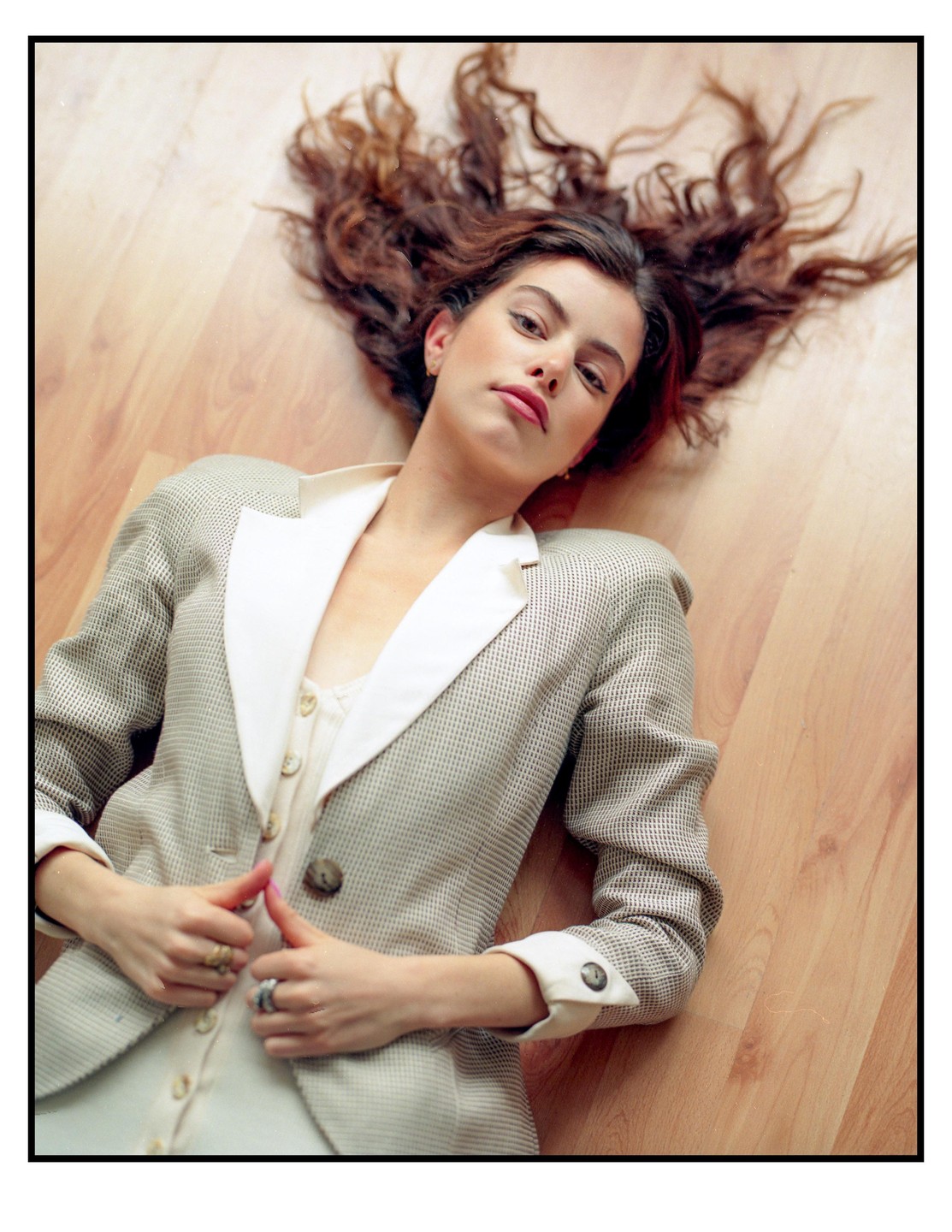 A woman with long, curly hair lies on a wooden floor, looking up at the viewer.
