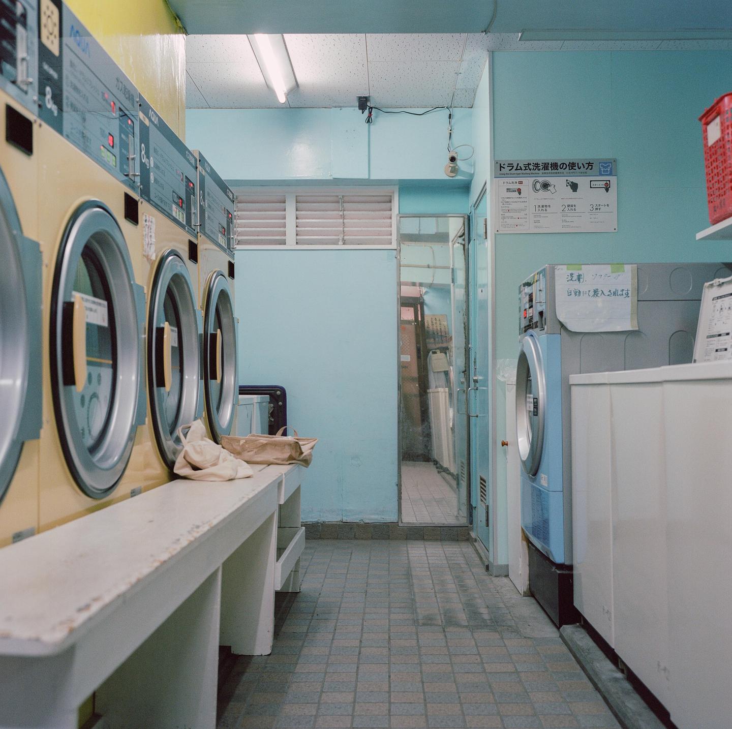 A row of washing machines lines a narrow room with light blue walls and a tiled floor.