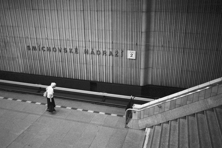 A woman walks along a subway platform next to a wall with the station name and a sign for track 2.