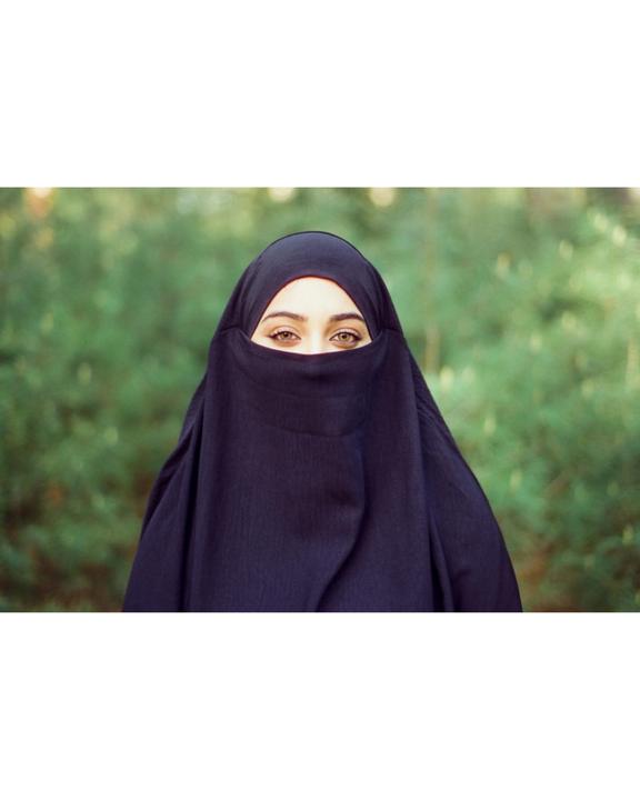 A woman wearing a niqab looks directly at the viewer with a green, out-of-focus background.