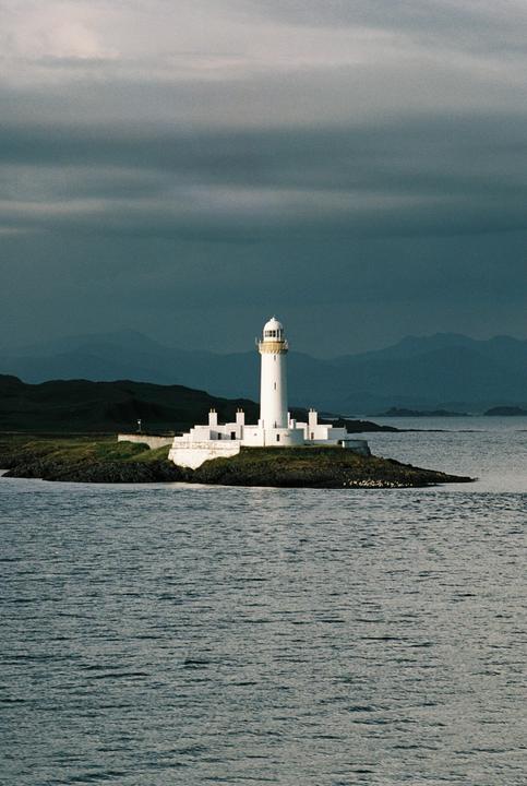 A white lighthouse stands on a small island surrounded by water under a dramatic sky.
