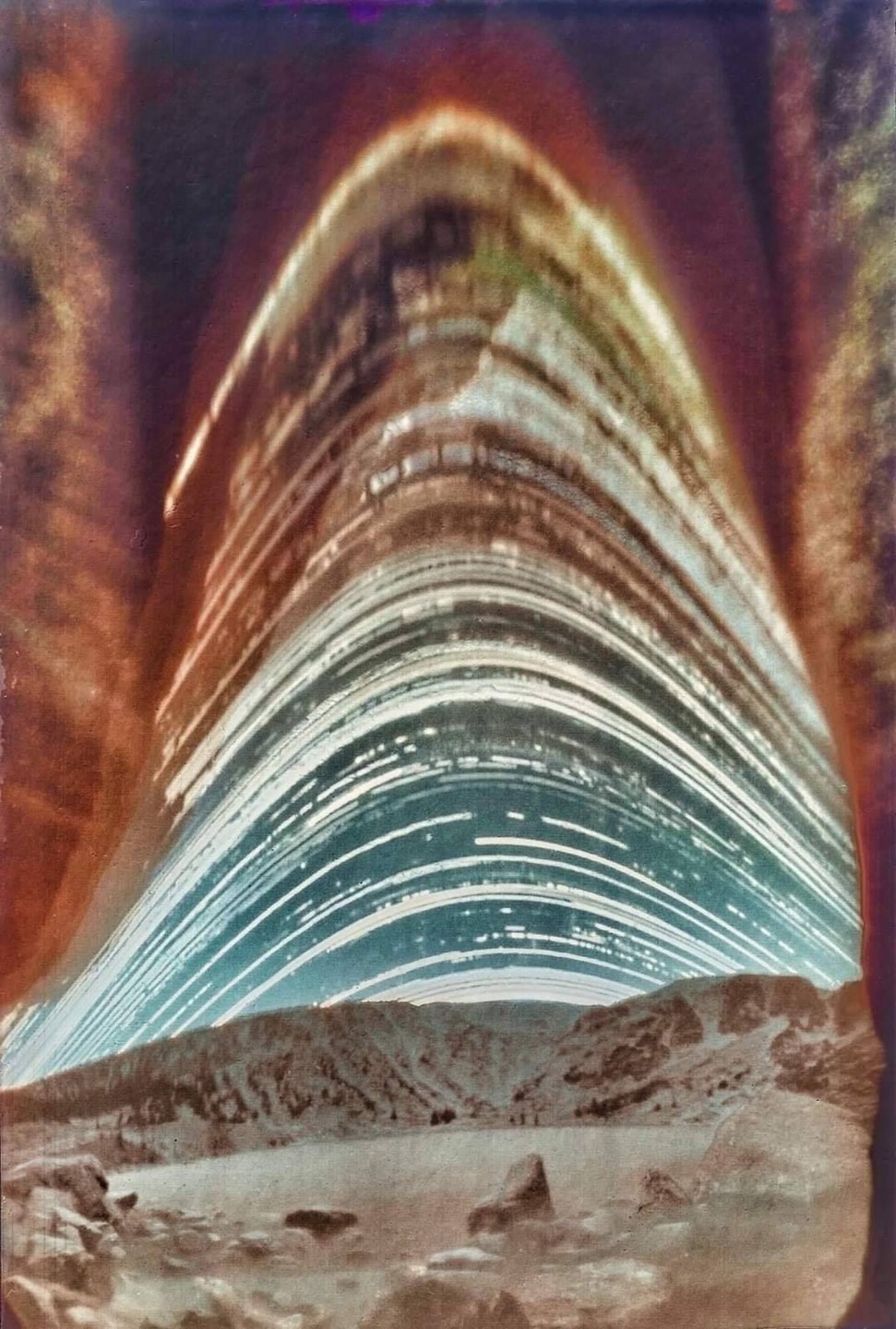 A long exposure photograph shows the sun's path over a mountain landscape with a lake.