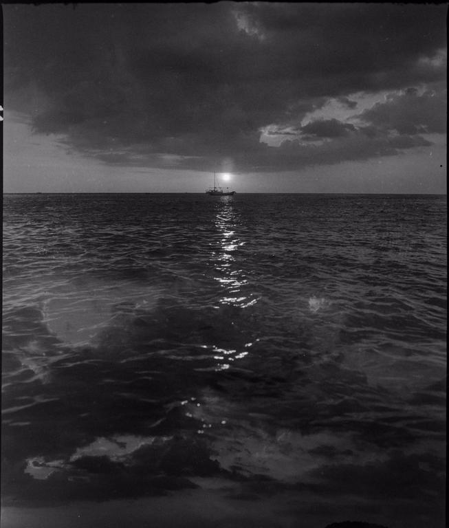 A boat is visible on the horizon with the sun setting behind it, casting a reflection on the water.