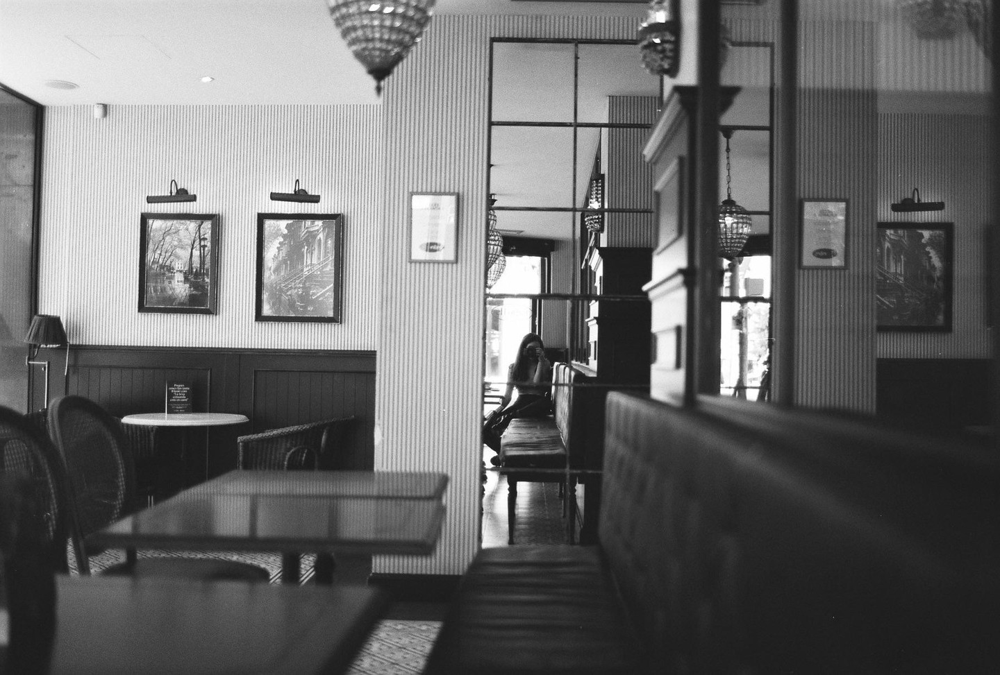 A woman is visible in a mirror reflection in a cafe with tables and chairs.