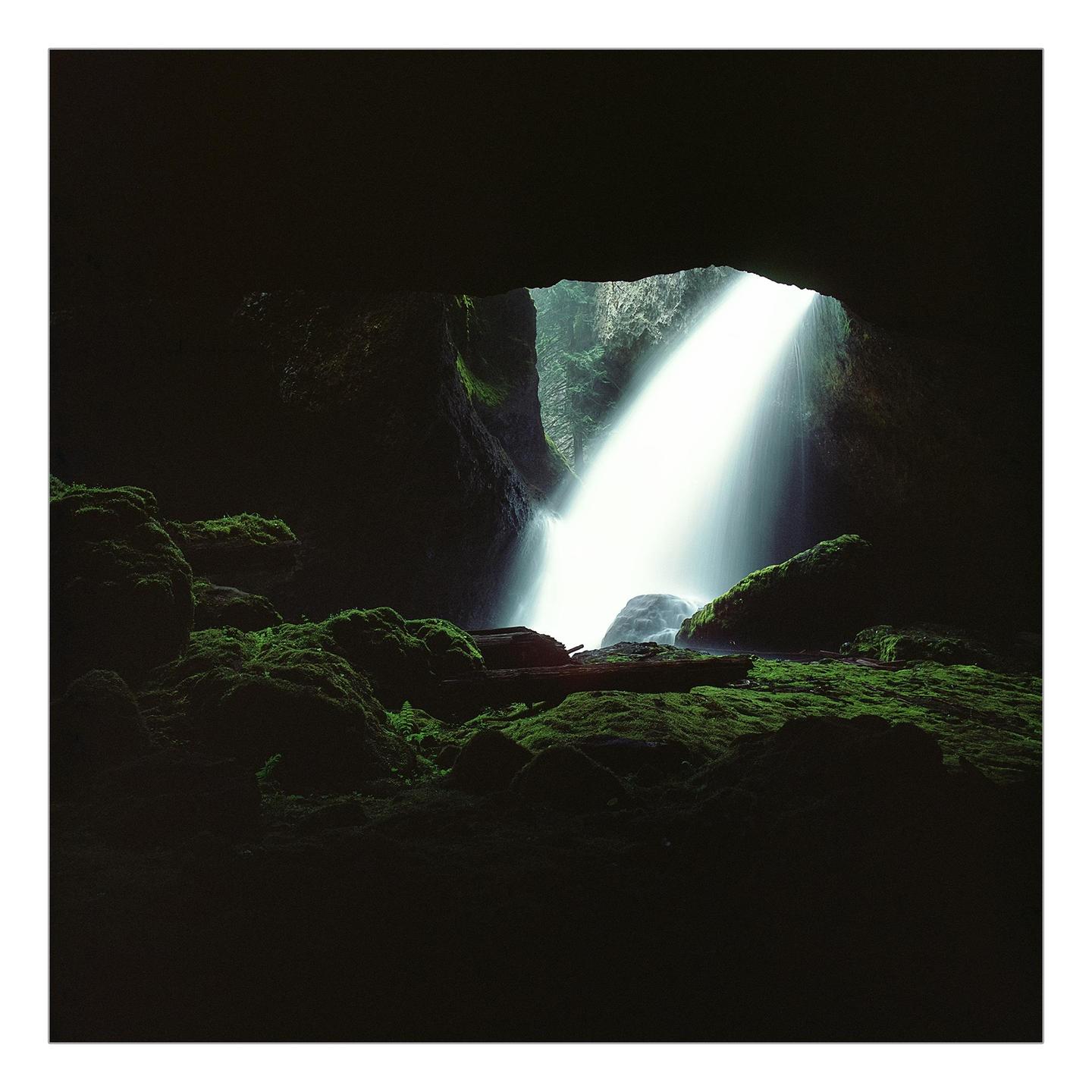 A waterfall cascades into a dark grotto covered in moss.