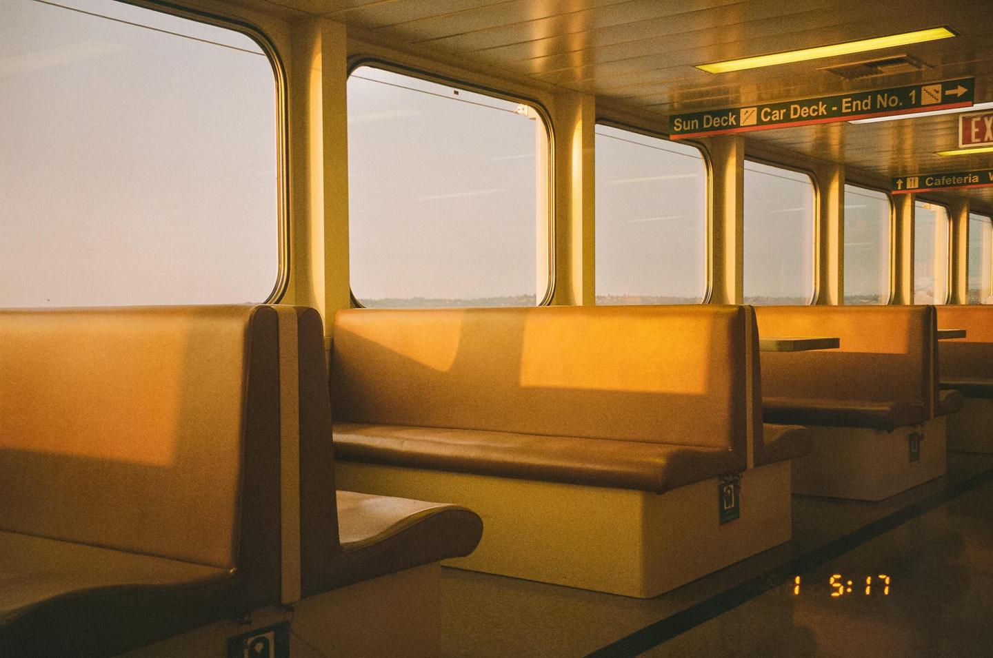 The interior of a ferry shows rows of empty seats and windows looking out onto a hazy sky.