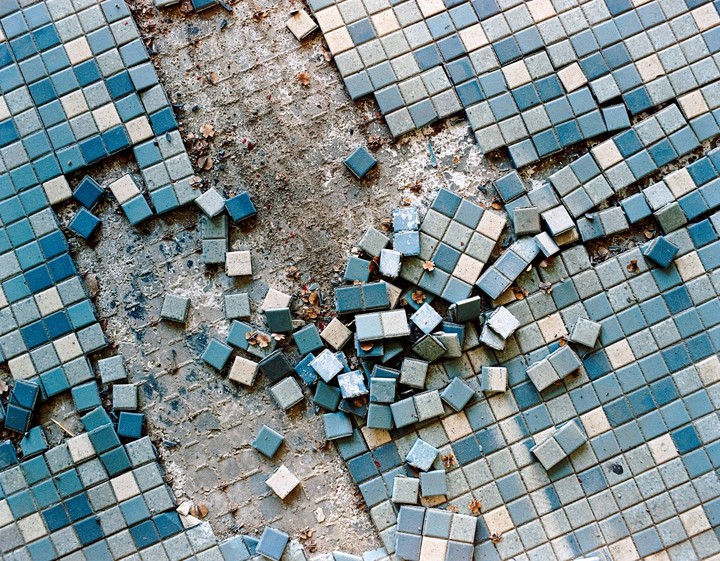 A close-up overhead view shows a floor of broken blue and white tiles with some scattered on the ground.