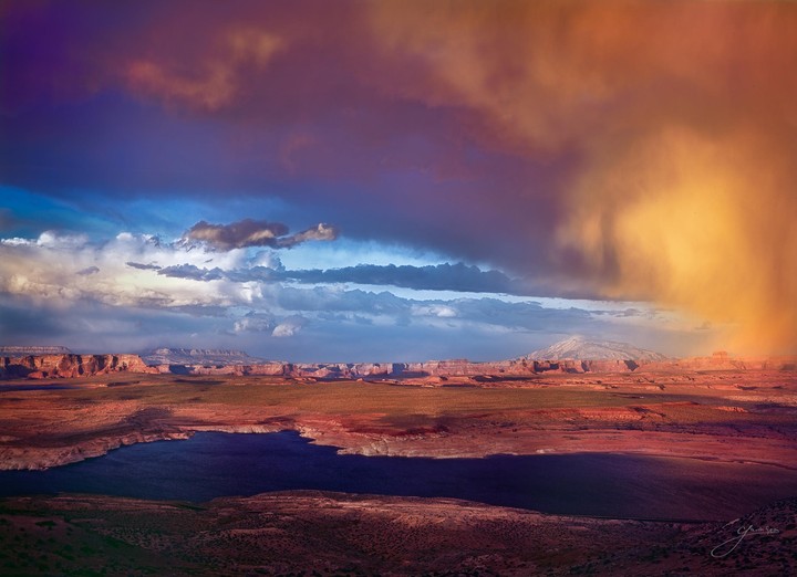 A dramatic sky with storm clouds and a golden light over a vast desert landscape with a lake and distant mountains.