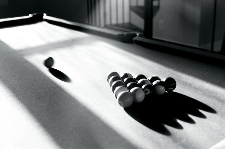 A cue ball and racked billiard balls cast long shadows on a pool table.