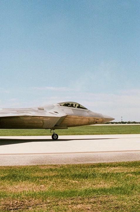 A fighter jet is parked on an airfield with green grass and a clear blue sky.