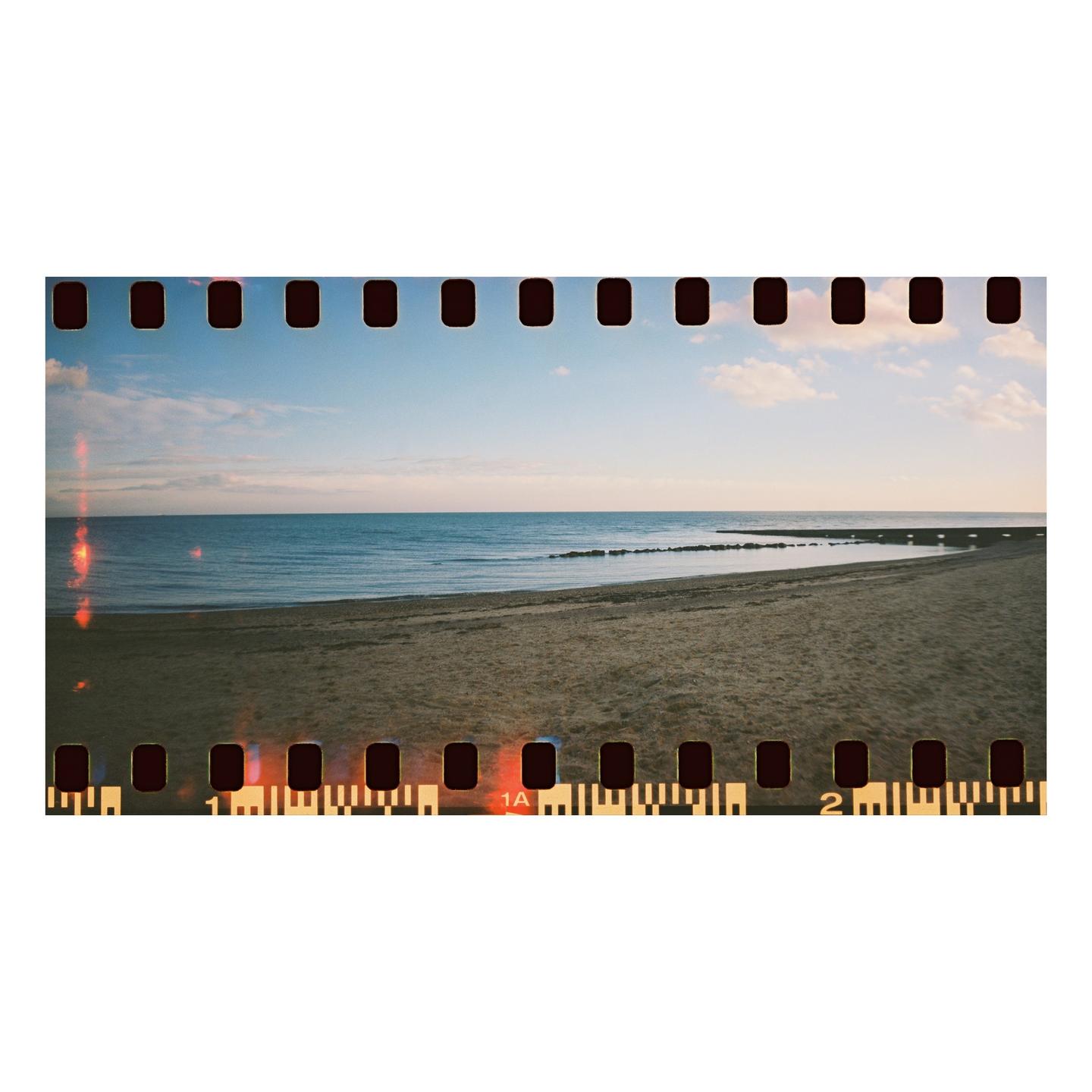 A sandy beach meets the ocean under a partly cloudy sky, with a pier visible in the distance.
