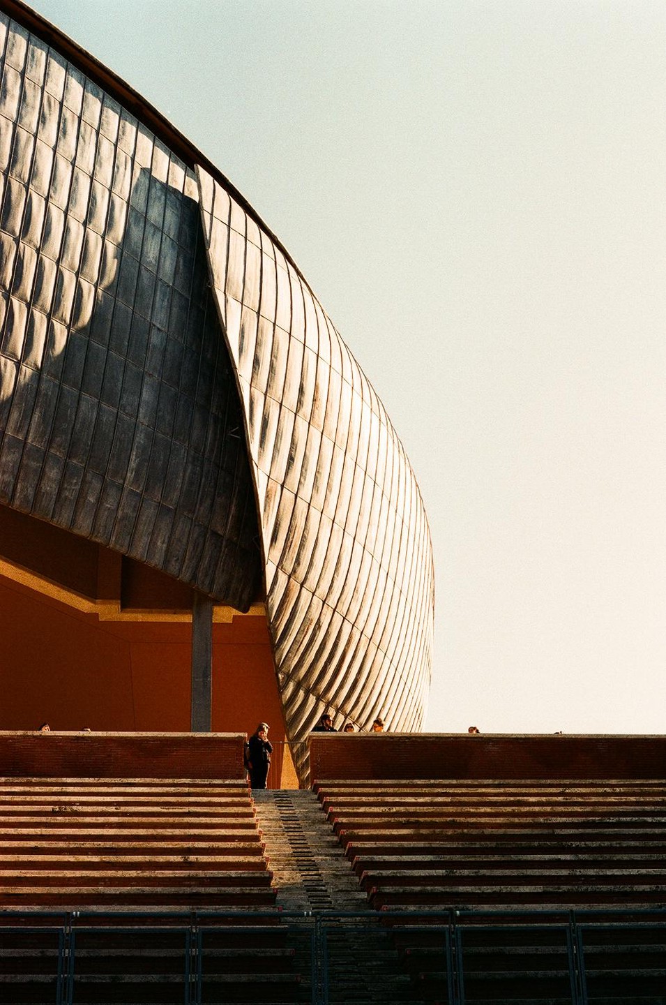 A person stands on a large set of concrete steps in front of a modern building with a curved, textured facade.