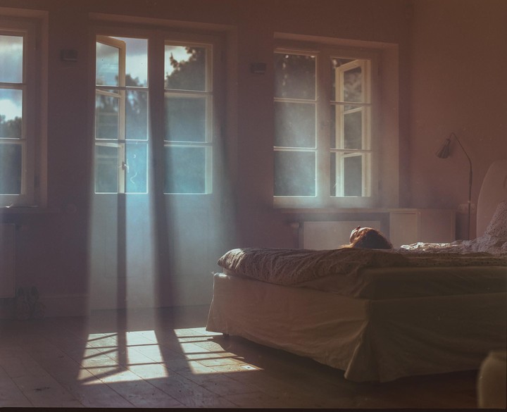 Sunlight streams through an open window onto a bed where a person is lying.