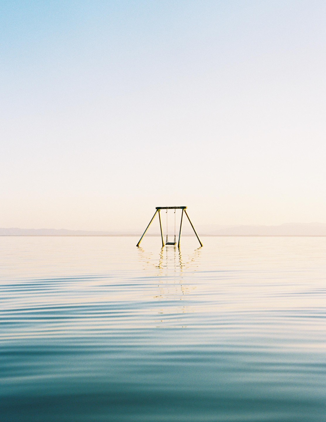 A swing set stands in the middle of a body of water under a clear sky.