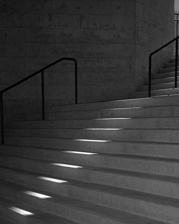 Sunlight casts shadows on a concrete staircase with black railings.