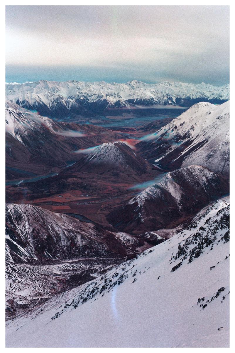 A vast mountain range with snow-capped peaks and a valley below is visible under a cloudy sky.