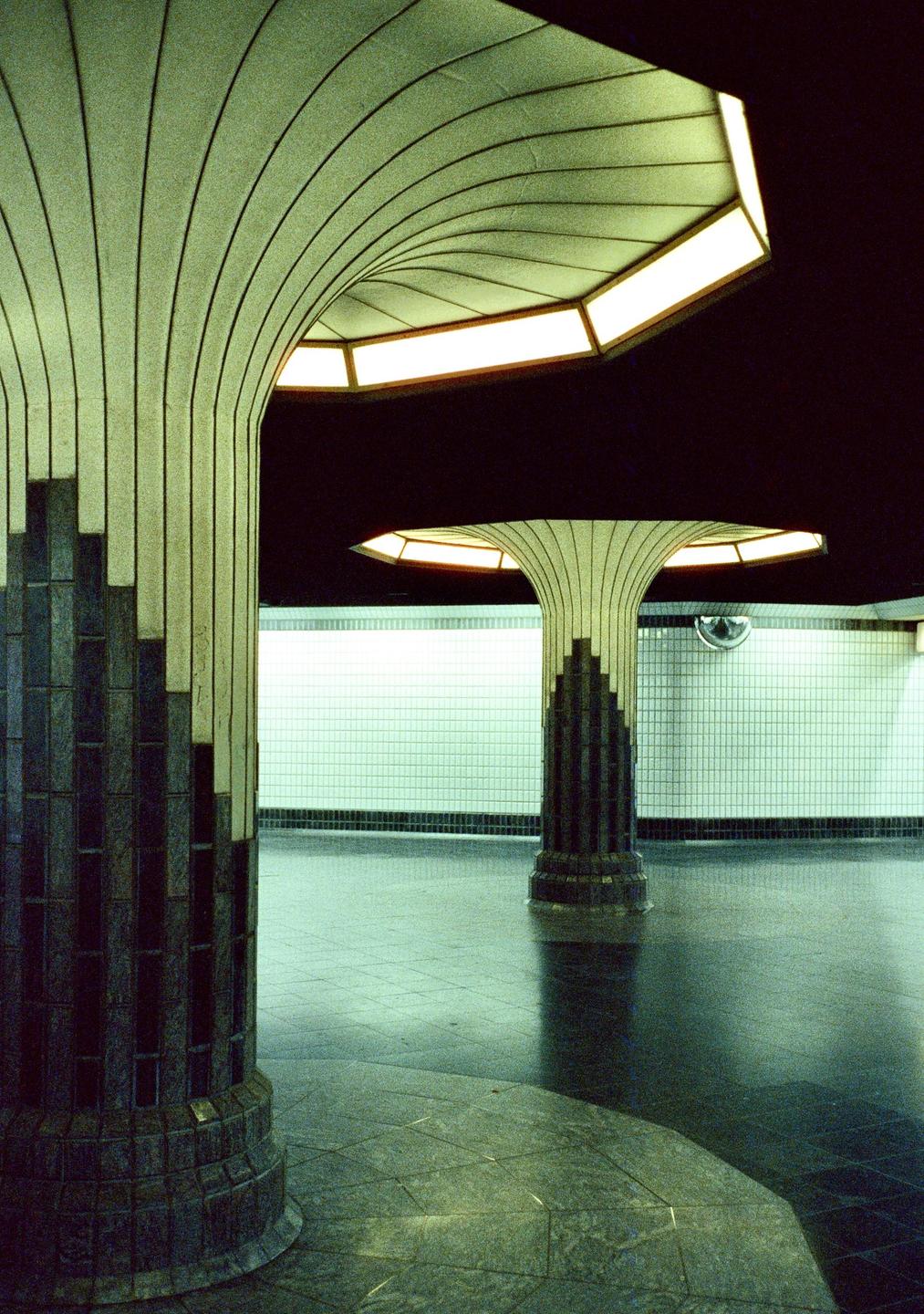 Two decorative columns with illuminated tops stand in a subway station with tiled walls.