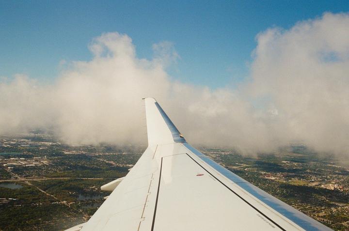 An airplane wing is visible above a landscape of clouds and a city.