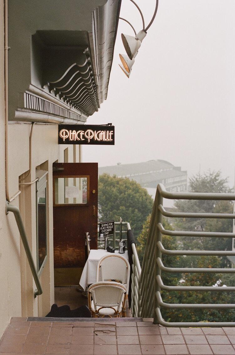 A restaurant balcony with a table and chairs is visible from a tiled staircase, with a hazy city in the background.