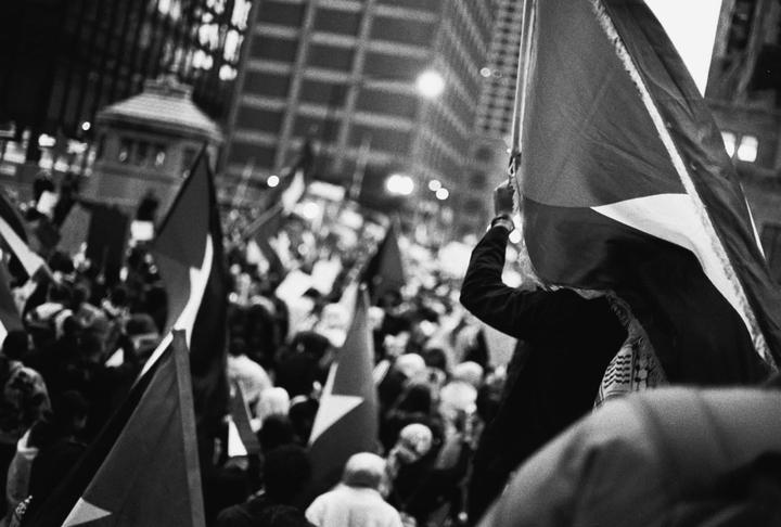 A crowd of people holding flags are gathered on a city street at night.