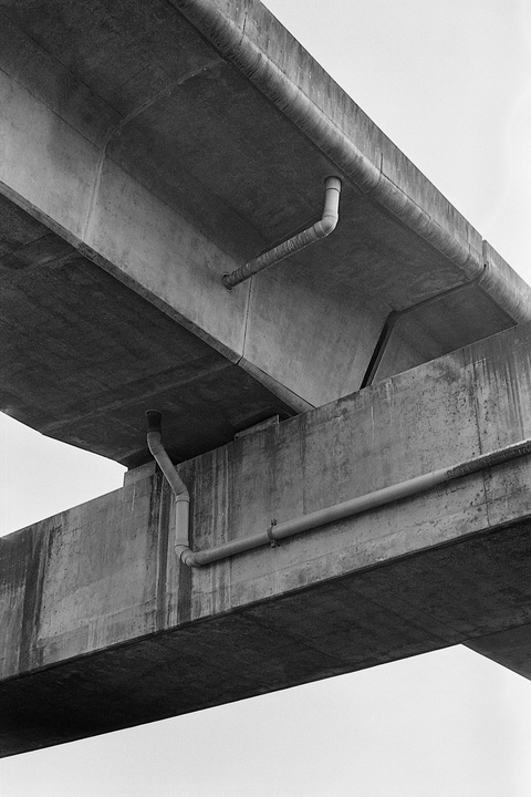 Two concrete overpasses with pipes running along them are shown from below.