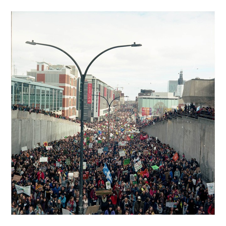 A large crowd of people are protesting in a city street, many holding signs and flags.