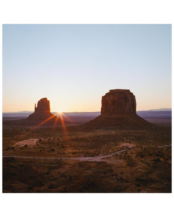 The sun rises between two large rock formations in a desert landscape.