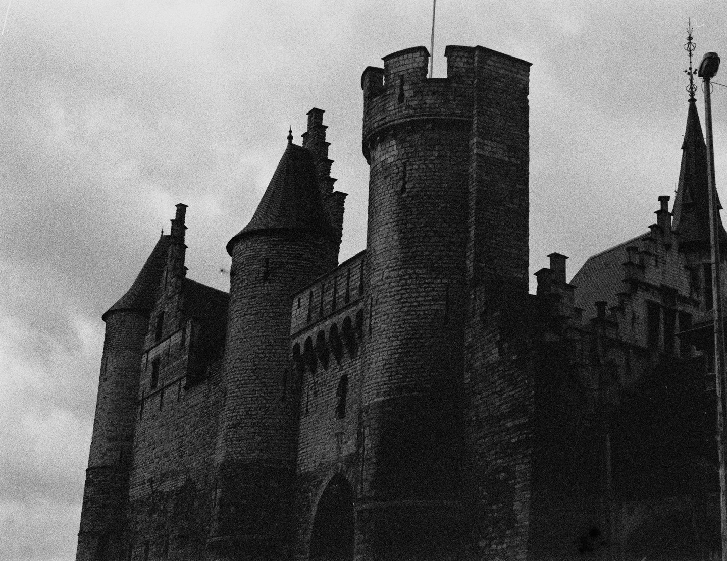 A large stone castle with multiple towers and turrets stands against a cloudy sky.