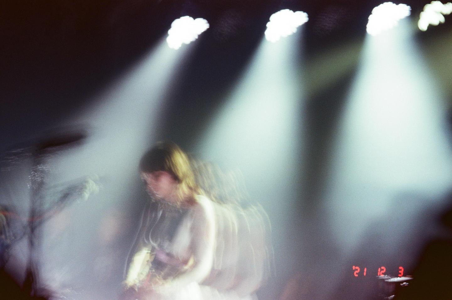 A woman with long hair is playing an instrument on a stage with bright spotlights and haze.