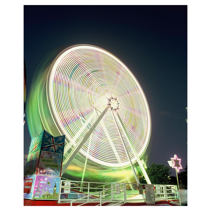 A long exposure shot captures a brightly lit Ferris wheel spinning at night, creating trails of light.