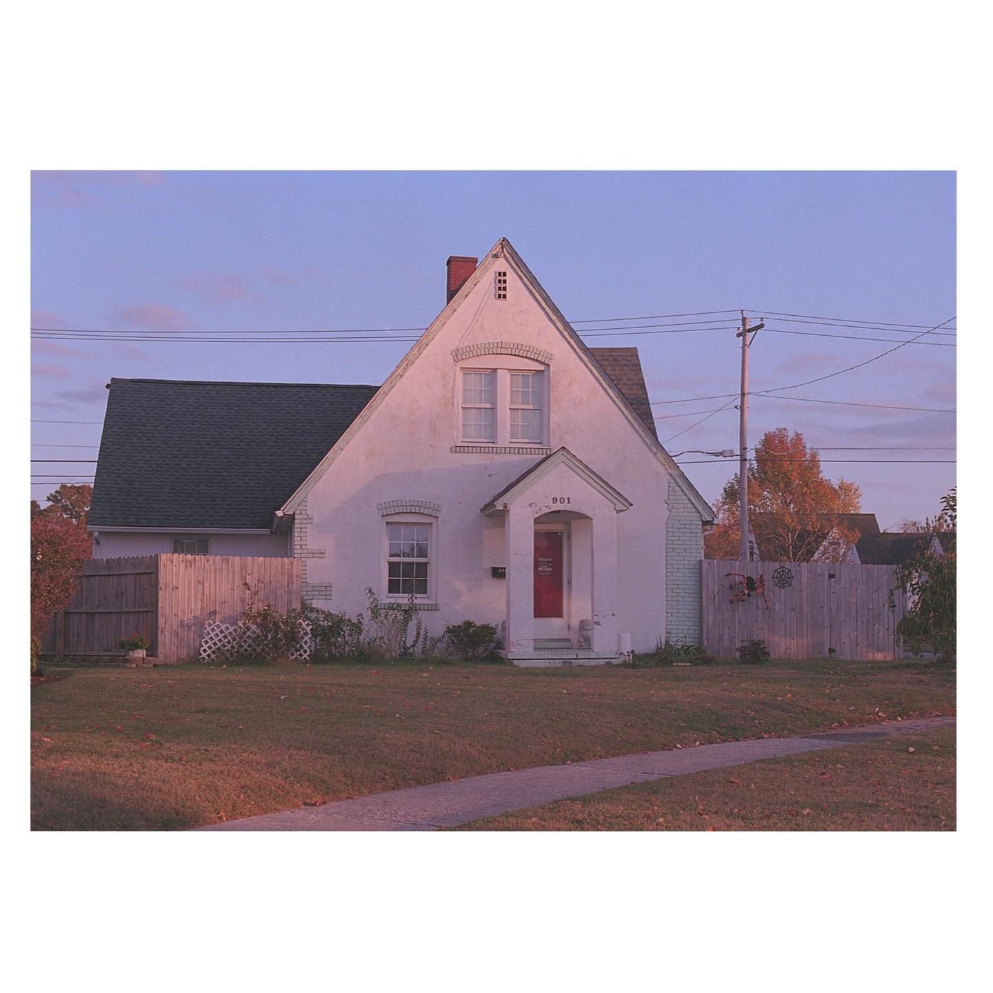 A white house with a red door and a green roof stands under a purple sky.