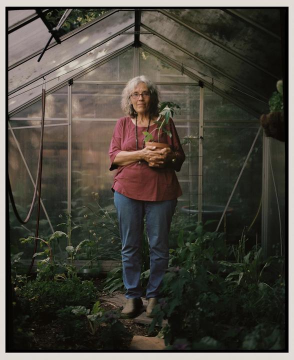 A woman stands in a greenhouse holding a potted plant.