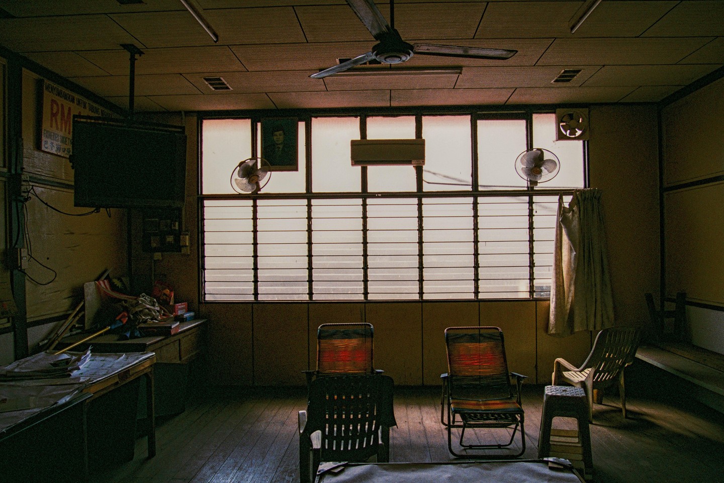 A room with a large window, ceiling fan, and several chairs is illuminated by natural light.