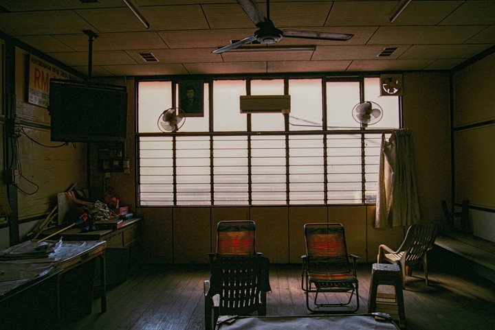 A room with a large window, ceiling fan, and several chairs is illuminated by natural light.