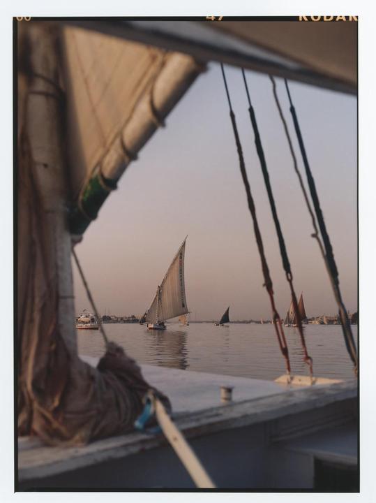 A view from a boat shows several sailboats on the water with a hazy sky in the background.