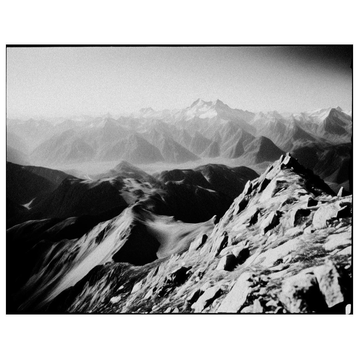 A rocky mountain ridge overlooks a valley filled with many mountains and a distant mountain range.