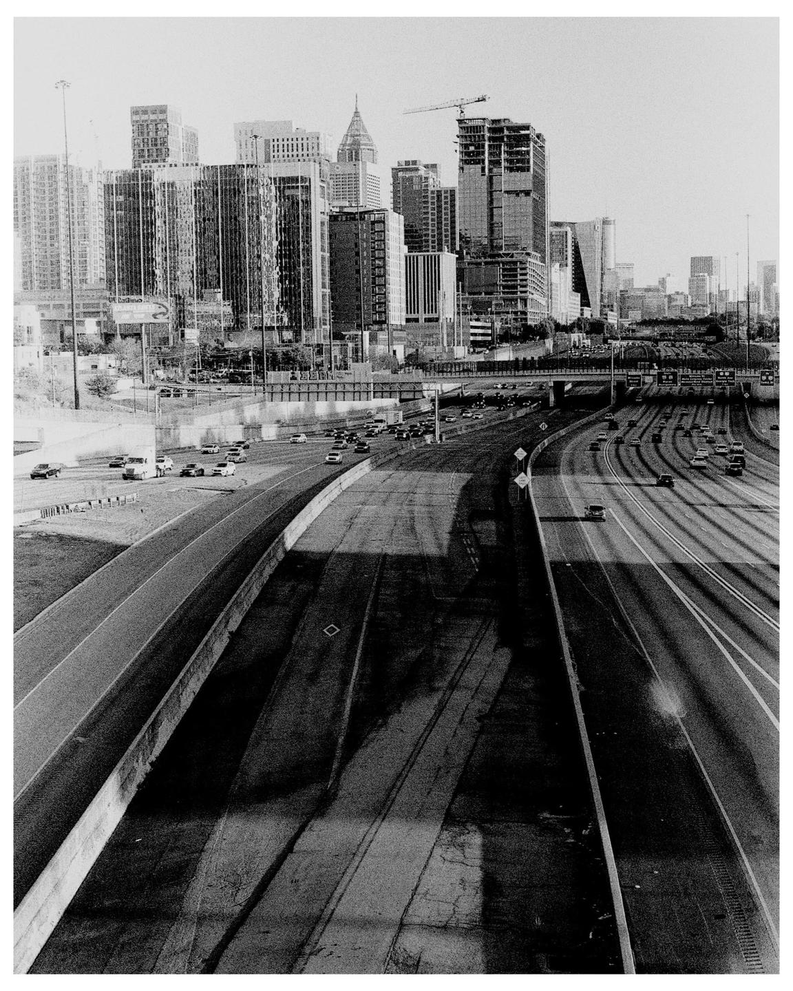 A black and white cityscape shows a highway with cars and tall buildings in the background.