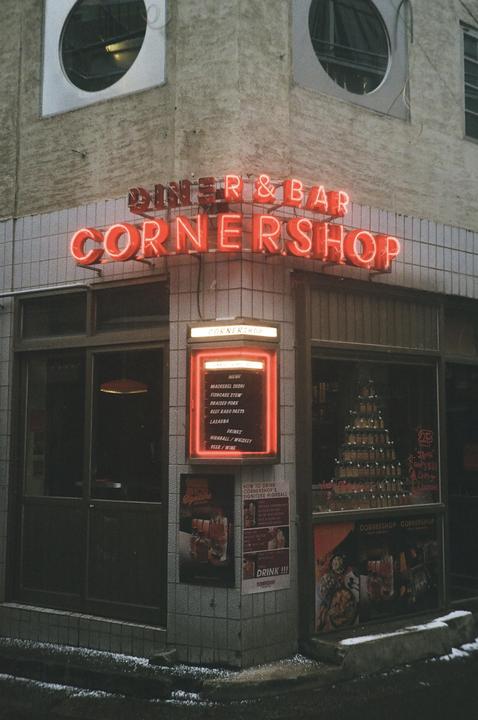A neon sign for a diner and bar called Cornershop illuminates a building at night.