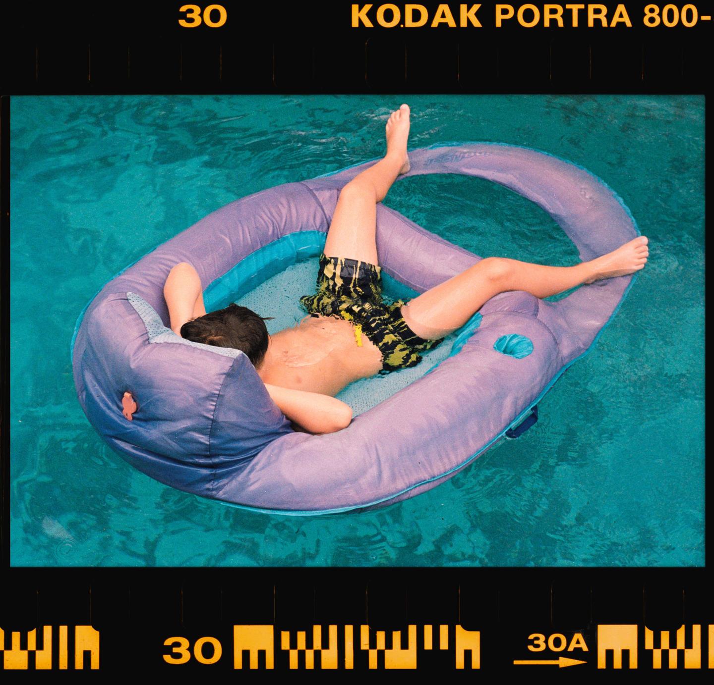 A boy floats on a purple inflatable raft in a swimming pool.