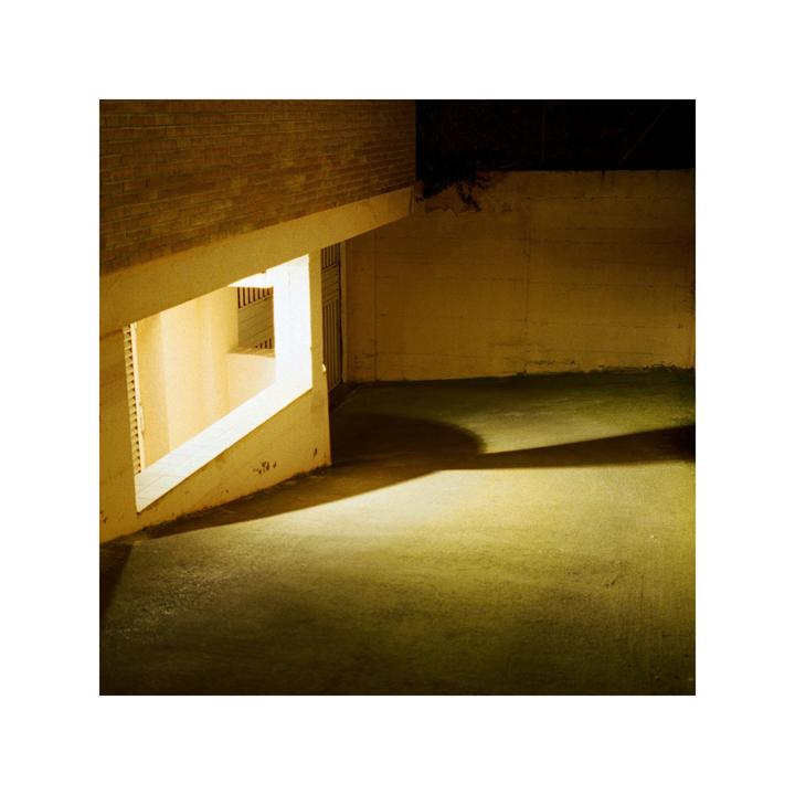 A brightly lit window casts a long shadow across a concrete floor at night.