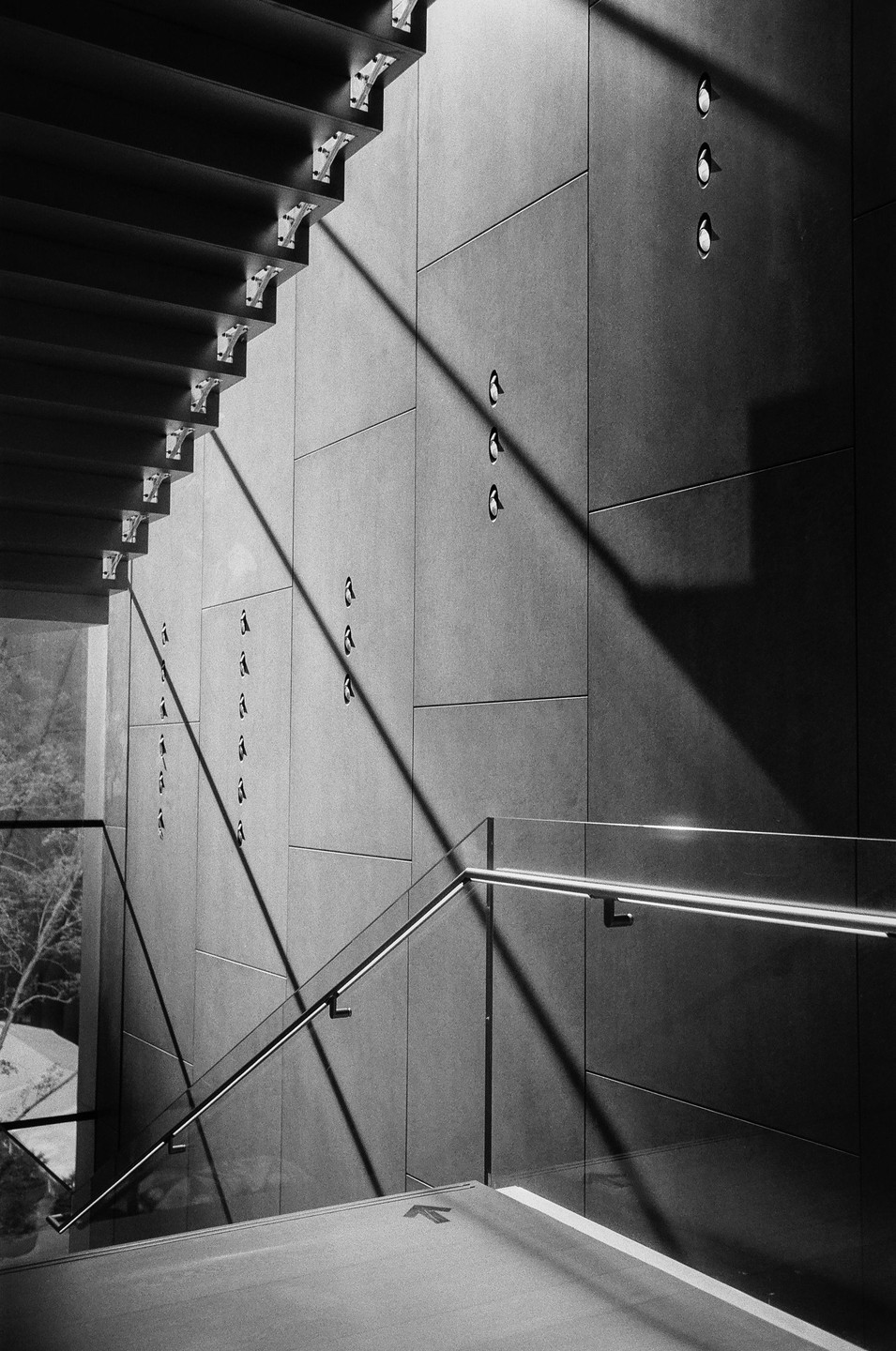 Sunlight casts strong diagonal shadows across a modern staircase and wall with small lights.