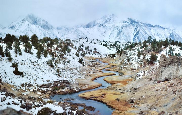 A winding river flows through a snowy valley with mountains in the background.