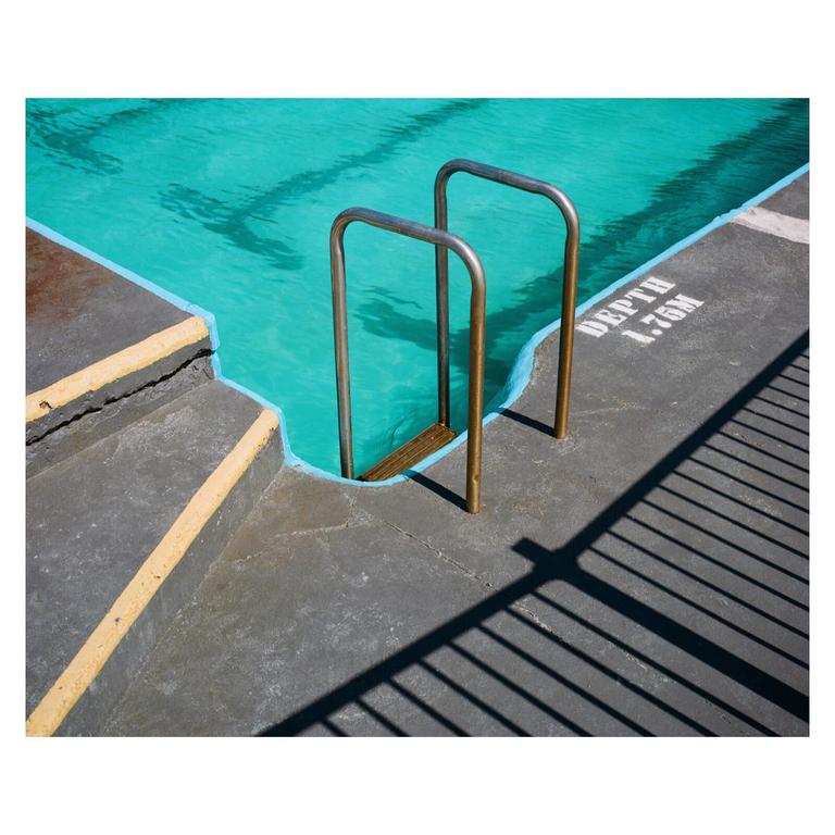 A swimming pool with turquoise water has a metal ladder and the word "DEPTH" painted on the concrete edge.