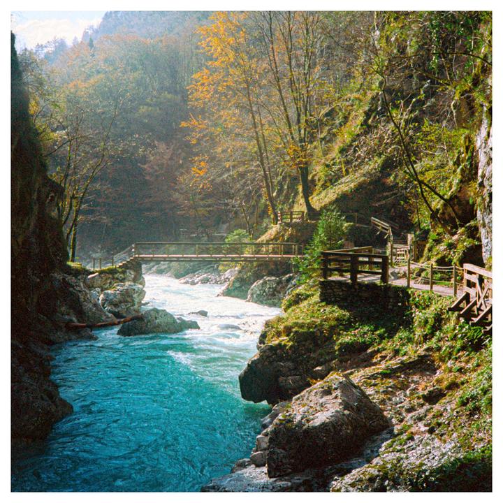 A turquoise river flows through a gorge with a wooden bridge and walkway.