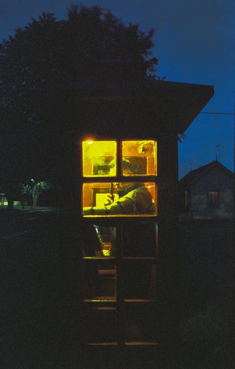 A person is visible through the illuminated windows of a phone booth at night.
