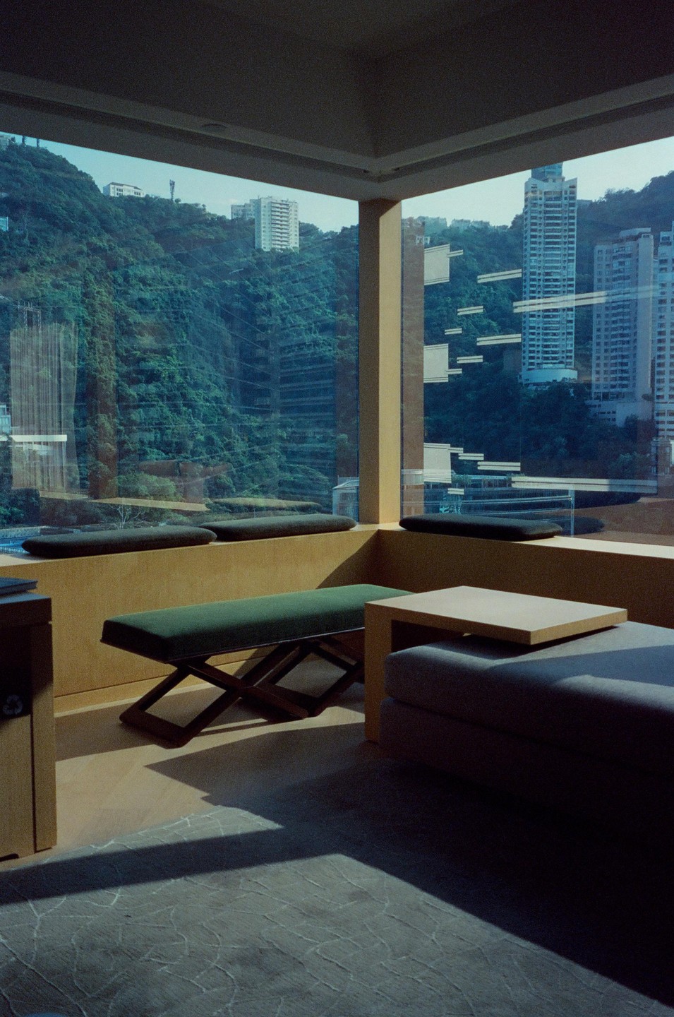 A modern room with large windows overlooks a lush green mountain with tall buildings.
