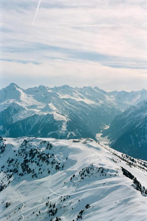 A vast mountain range covered in snow with a valley visible in the distance under a cloudy sky.