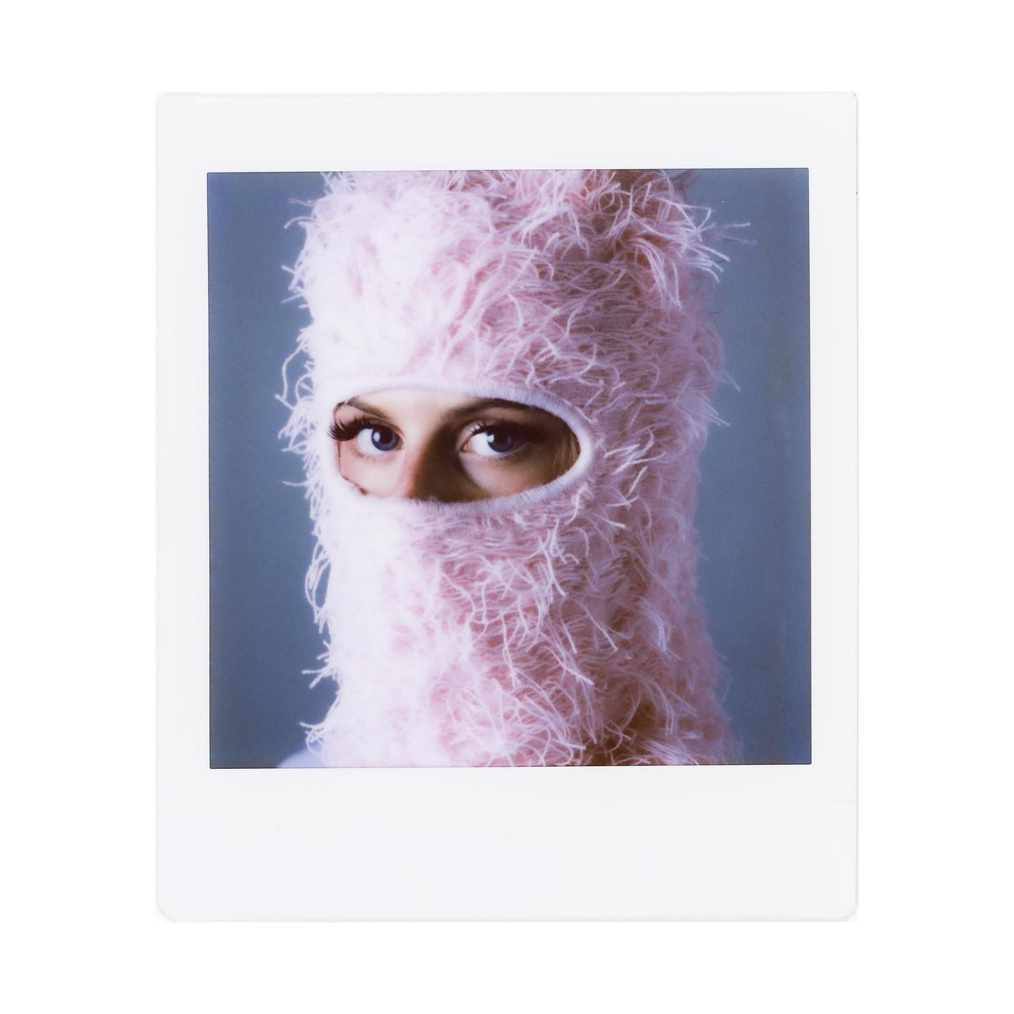 A woman wearing a pink fluffy balaclava looks directly at the viewer.